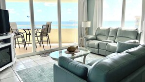 Un salón con sofá, mesa de centro y televisor. Hay un balcón con vista a la playa.
