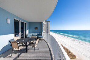 Un balcón con mesa y sillas, con vista a una playa de arena blanca y agua azul.