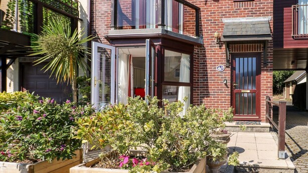 Una casa a due piani in mattoni con un balcone, un'antenna parabolica e un giardino pieno di piante e fiori.