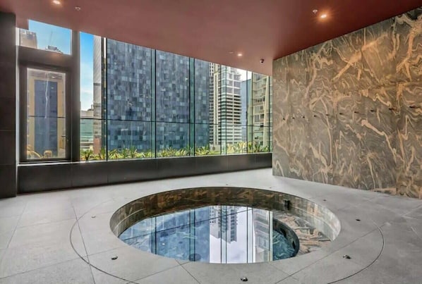 Una piscina interior moderna con cerramiento de vidrio, amplias ventanas que ofrecen vistas de la ciudad y una pared de mármol.