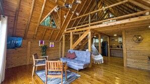 Un intérieur spacieux en bois, avec un plafond haut, un canapé, un fauteuil, une chaise suspendue et un téléviseur fixé au mur.