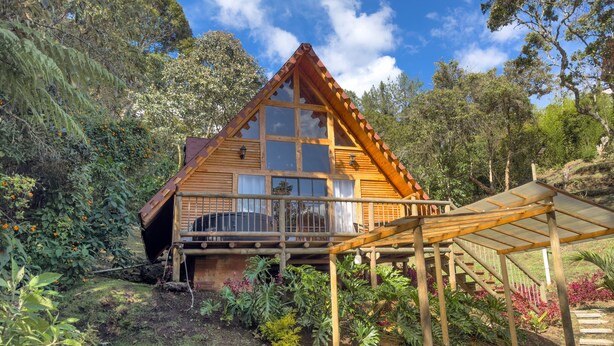 Une cabane en bois dotée d’un balcon, entourée d’une végétation luxuriante et surplombant un ciel dégagé.