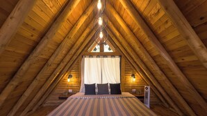 Une chambre mansardée chaleureuse avec un plafond en bois incliné, un lit avec une literie à rayures et une petite table de chevet avec une lampe.