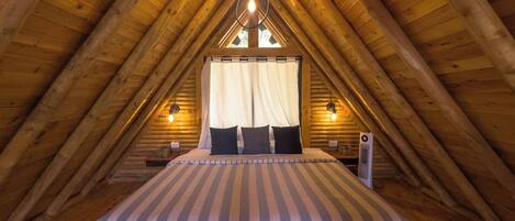Une chambre mansardée chaleureuse avec un plafond en bois incliné, un lit avec une literie à rayures et une petite table de chevet avec une lampe.