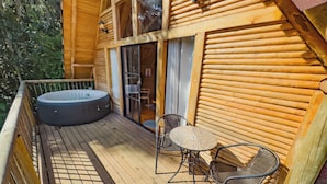 Une terrasse en bois avec un jacuzzi, deux fauteuils en osier et une porte vitrée donnant sur un espace intérieur.