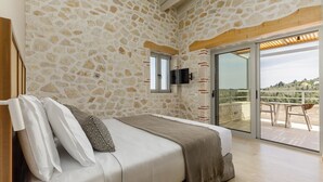 Een slaapkamer met een stenen muur, een bed met kussens, een aan de muur bevestigde televisie en een schuifdeur naar een buitenruimte.