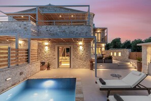 Une maison moderne à deux étages, avec une façade en pierre, une piscine et des espaces de détente en plein air.