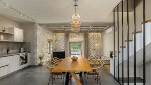 Een moderne keuken met stenen muren, een eethoek met een houten tafel en rieten stoelen, en een trap met zwarte leuningen.