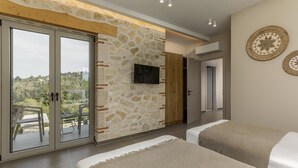 Een slaapkamer met twee bedden, een stenen muur, een televisie en een balkon met uitzicht op groen.