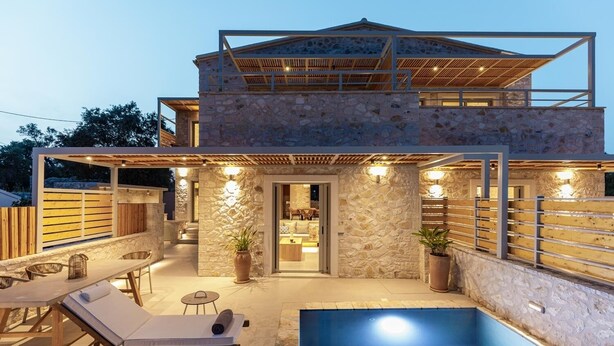 Une maison en pierre à deux étages, dotée d’une piscine, d’un espace salon extérieur et d’un patio couvert.