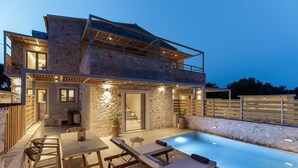Une maison en pierre à deux étages, dotée d’une piscine, d’un espace salon extérieur et d’un escalier menant à l’étage supérieur.