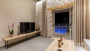 Un salon moderne avec un téléviseur à écran plat, un banc en bois, une orchidée en pot et un mur en pierre.