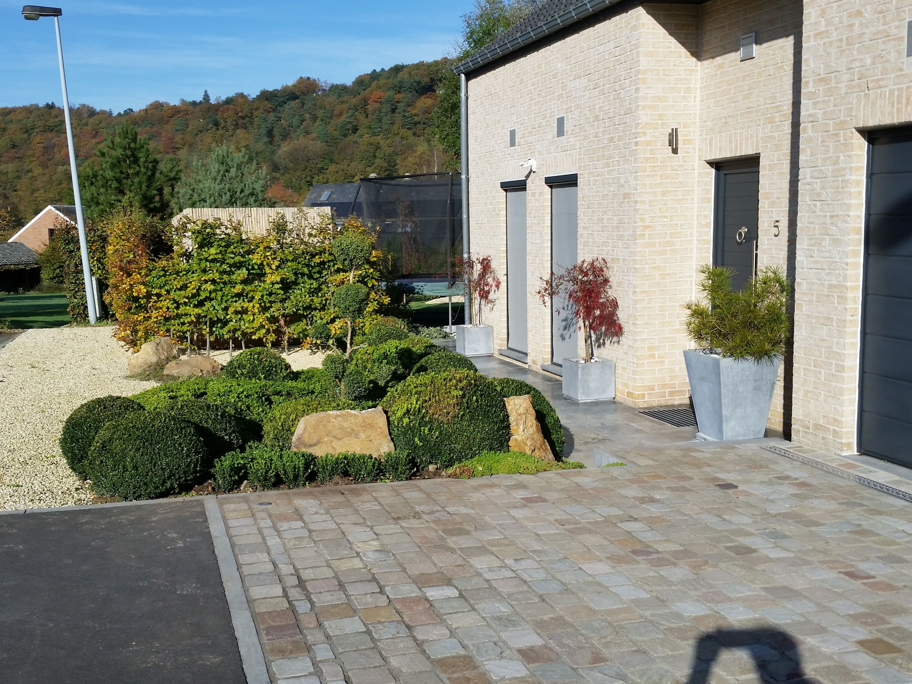 A building with a brick facade, a paved entrance, and a landscaped garden with shrubs and a rock feature.