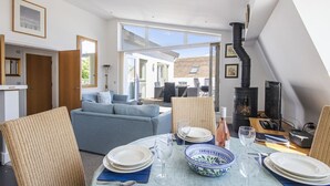 A dining area with a table set for four, a sofa, and a fireplace. - Howells Mere 90, Crows Nest - Elevated Lake Views, Spa Access, Sleeps 4 (Somerford Keynes)