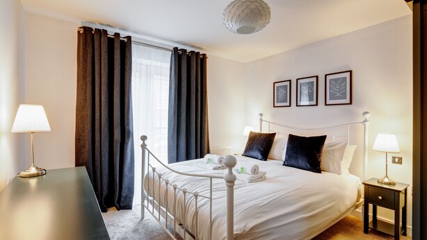 Una habitación de hotel con cama, mesitas de noche, un escritorio y un gran ventanal con cortinas.