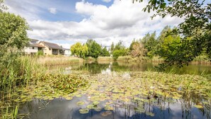 A serene lakeside setting with a building featuring a balcony and a view of the water. - Clearwater 67, Ortolan Villa (P) - Lakeside House, Hot Tub, Spa Access, Sleeps 8 (Somerford Keynes)