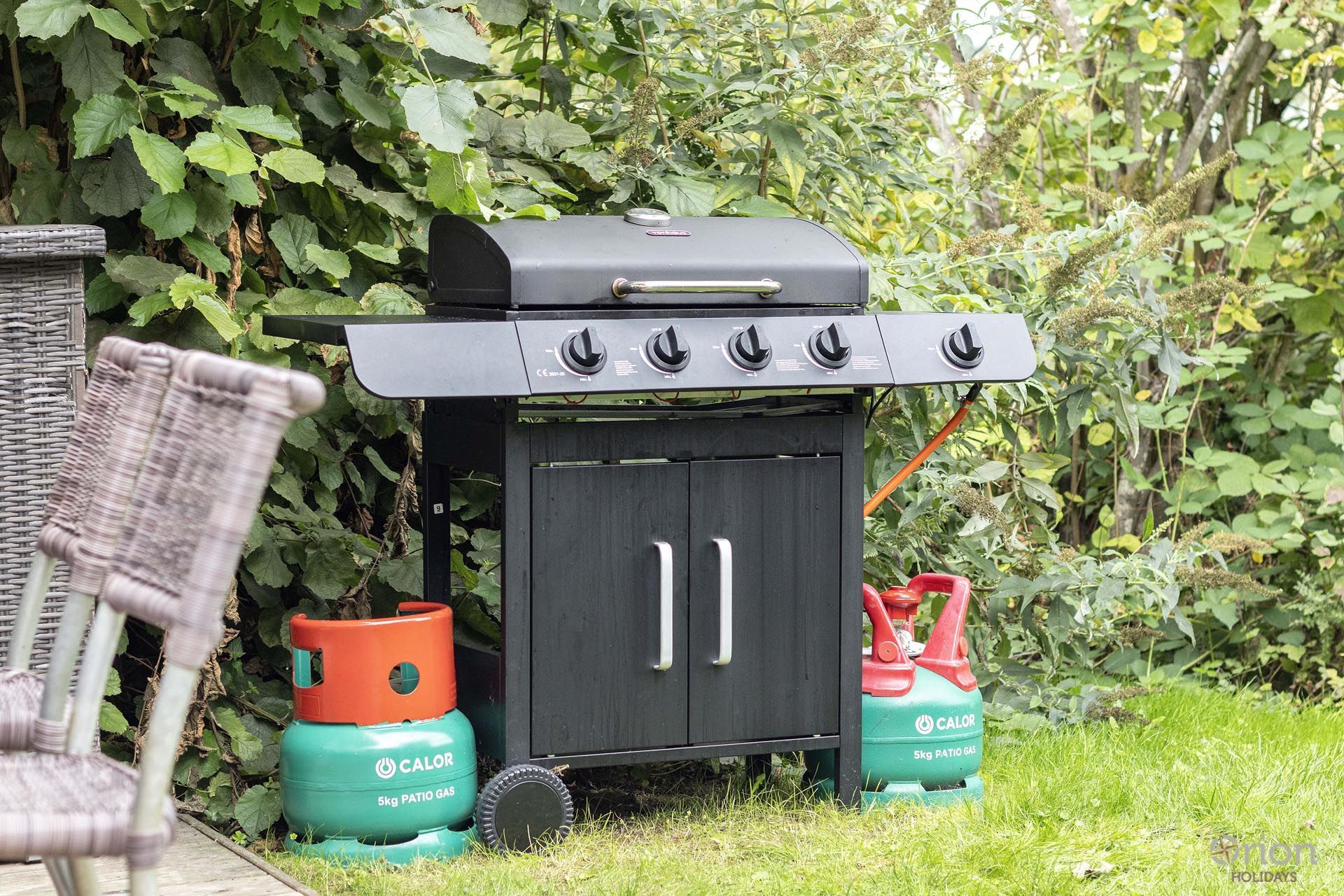 Un barbecue portable doté d'un meuble de rangement et de deux bouteilles de gaz.