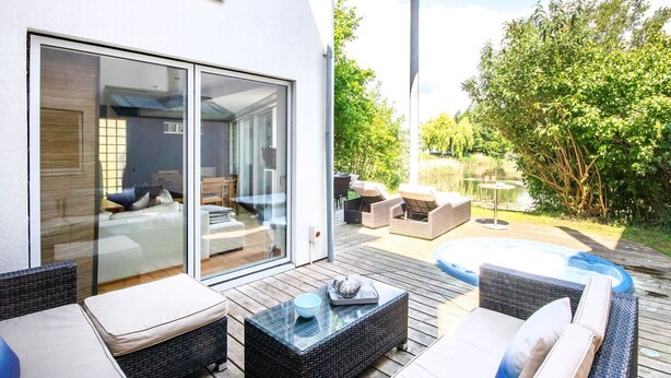 A modern outdoor living area with wicker furniture, a hot tub, and a glass-enclosed patio. - Clearwater 67, Ortolan Villa (P) - Lakeside House, Hot Tub, Spa Access, Sleeps 8 (Somerford Keynes)