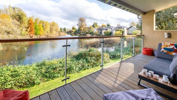 Ein Balkon mit Seeblick, umgeben von Herbstlaub, und eine Sitzecke mit Kissen und einem Tisch.