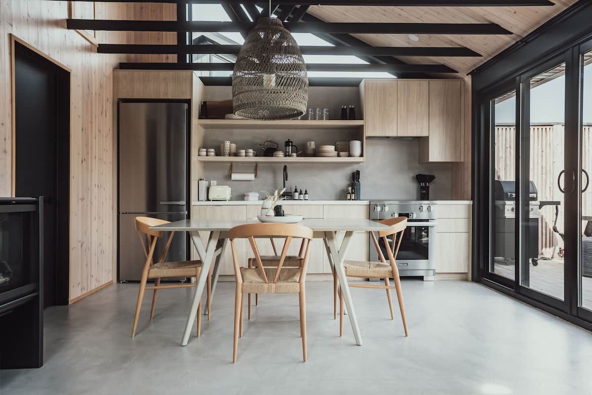 A modern kitchen with wooden cabinetry, a stainless steel refrigerator, and a dining area with a table and chairs.