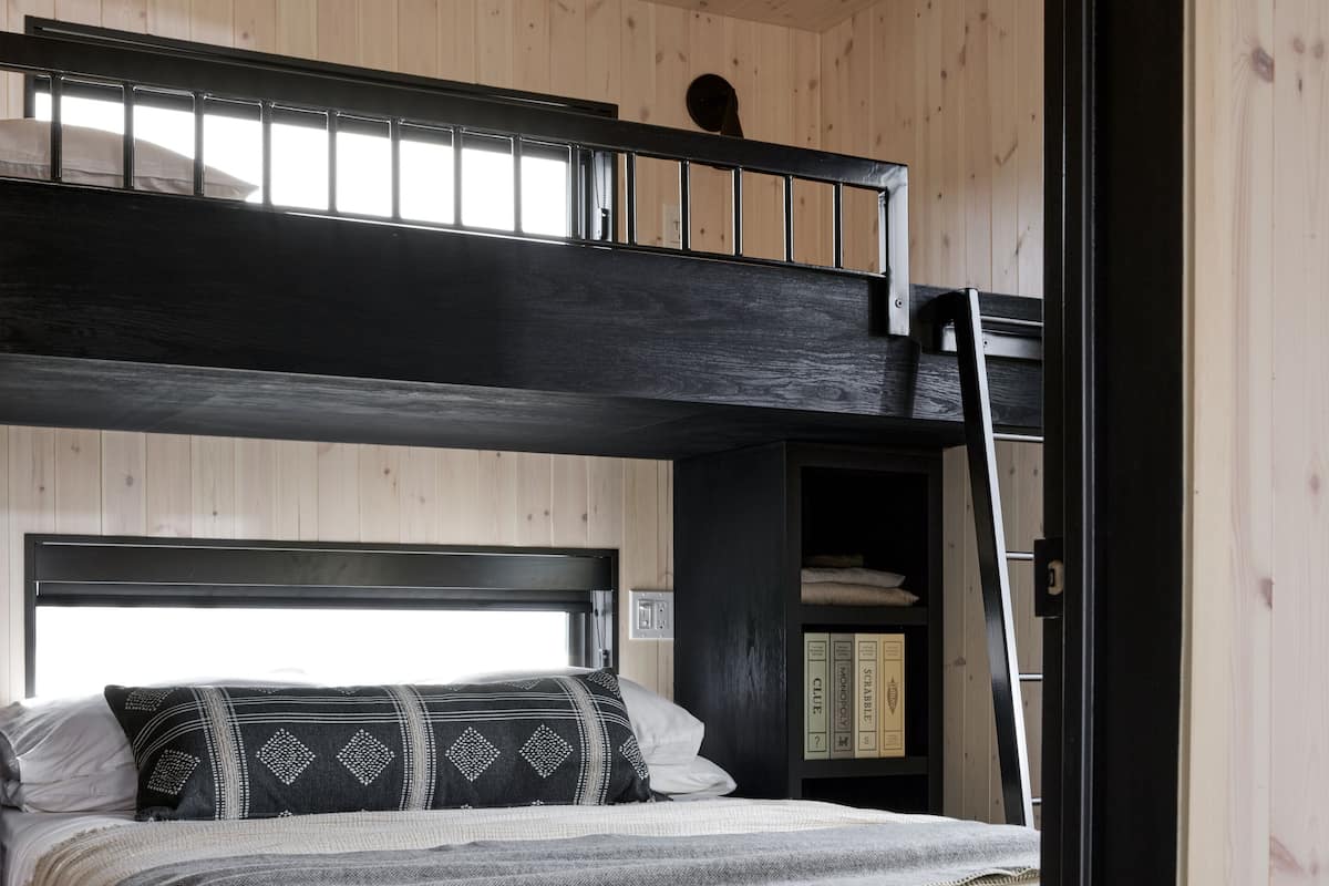 A bunk bed with a black headboard and a lower bed with a white headboard. There is a ladder leading to the upper bunk.
