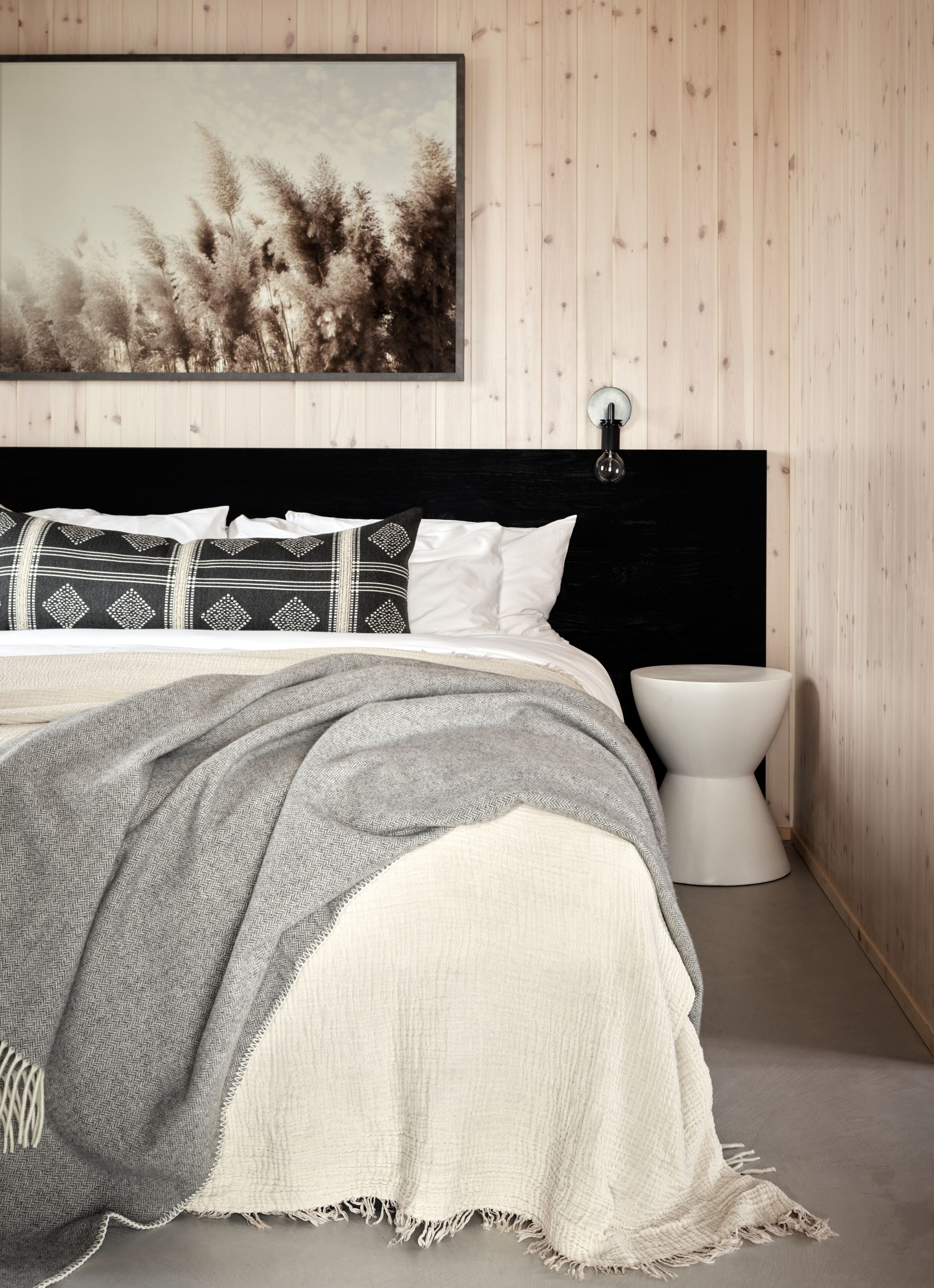 Une chambre à coucher comprenant un lit, une table de chevet, une lampe fixée au mur et un tableau encadré accroché au mur.