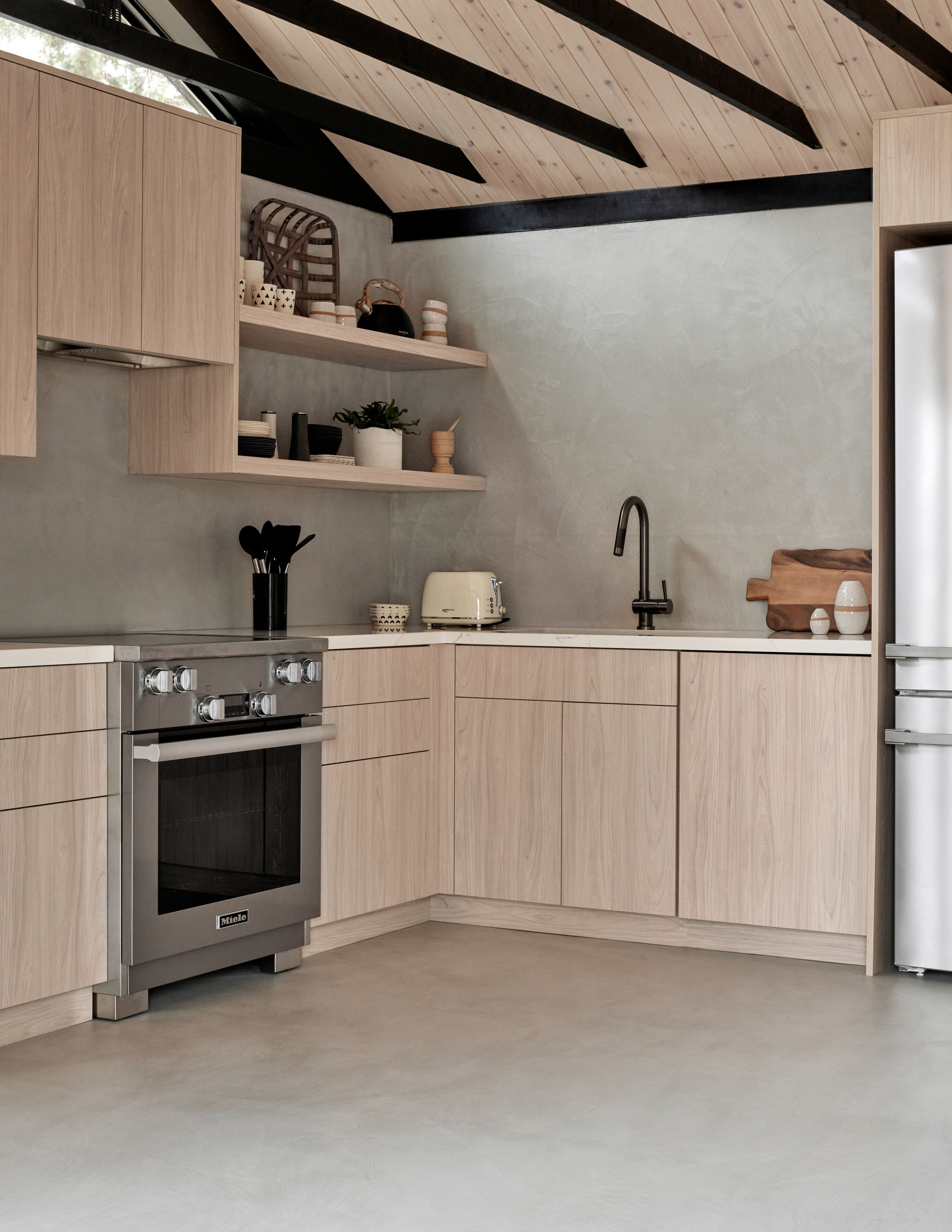 A modern kitchen with wooden cabinets, a built-in oven, and a stainless steel refrigerator.