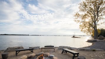 A lakeside seating area with benches and a fire pit.