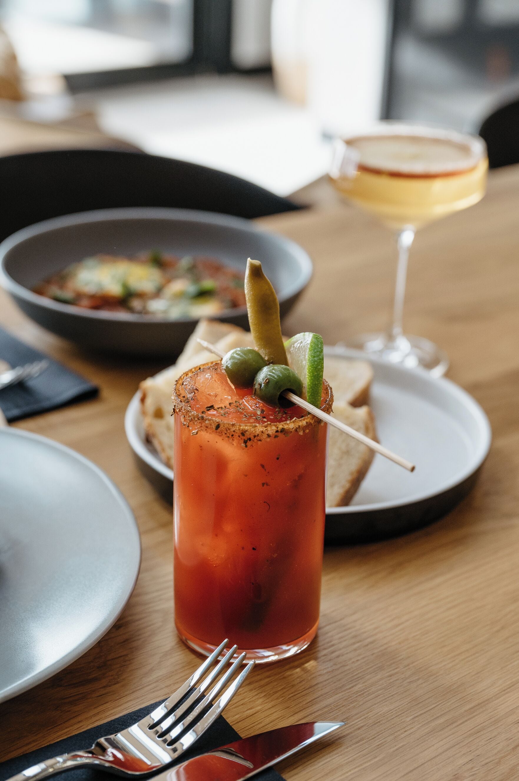 A dining table with a Bloody Mary, a glass of wine, and a plate of food.