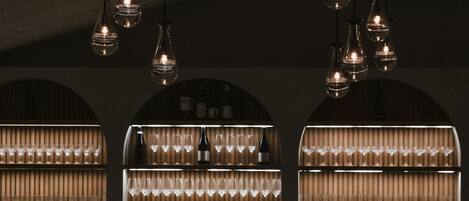 A bar area with a counter, stools, and shelves of bottles and glasses.