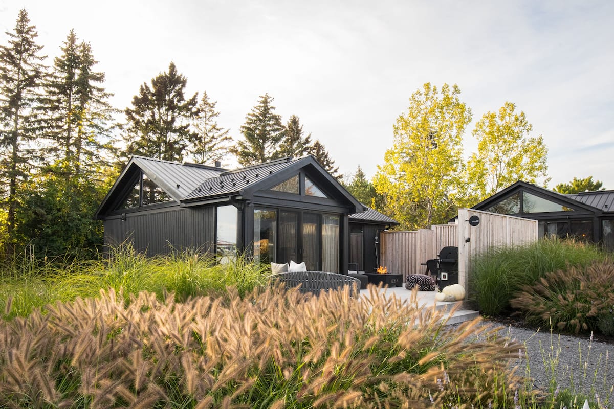 A modern house with a large glass window, surrounded by tall trees and a well-maintained garden.