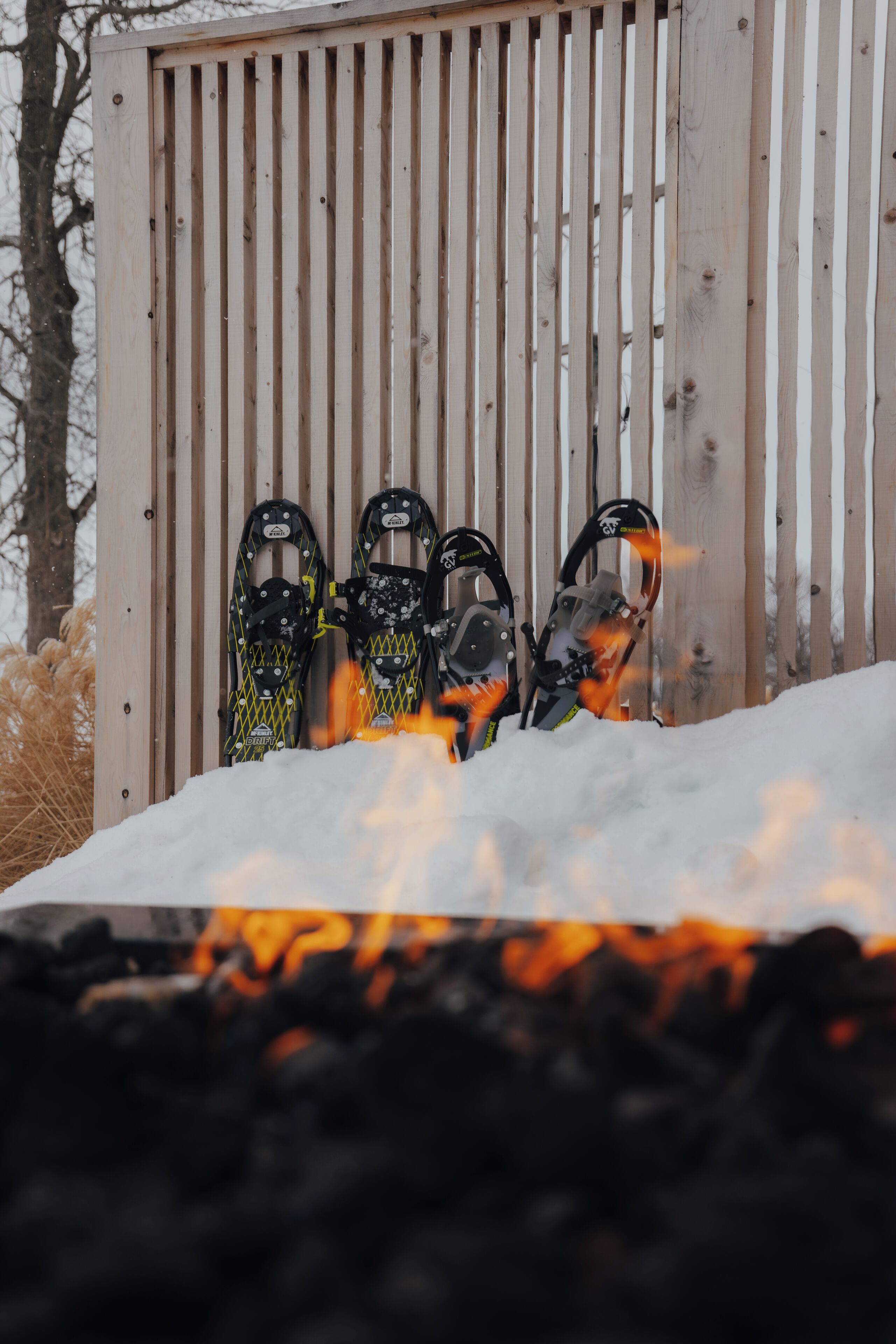 A row of snowshoes leaning against a wooden fence in a snowy setting.