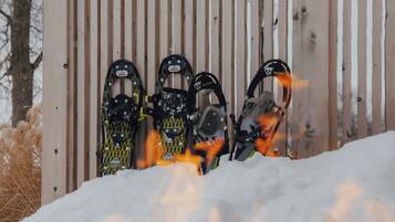A row of snowshoes leaning against a wooden fence in a snowy setting.