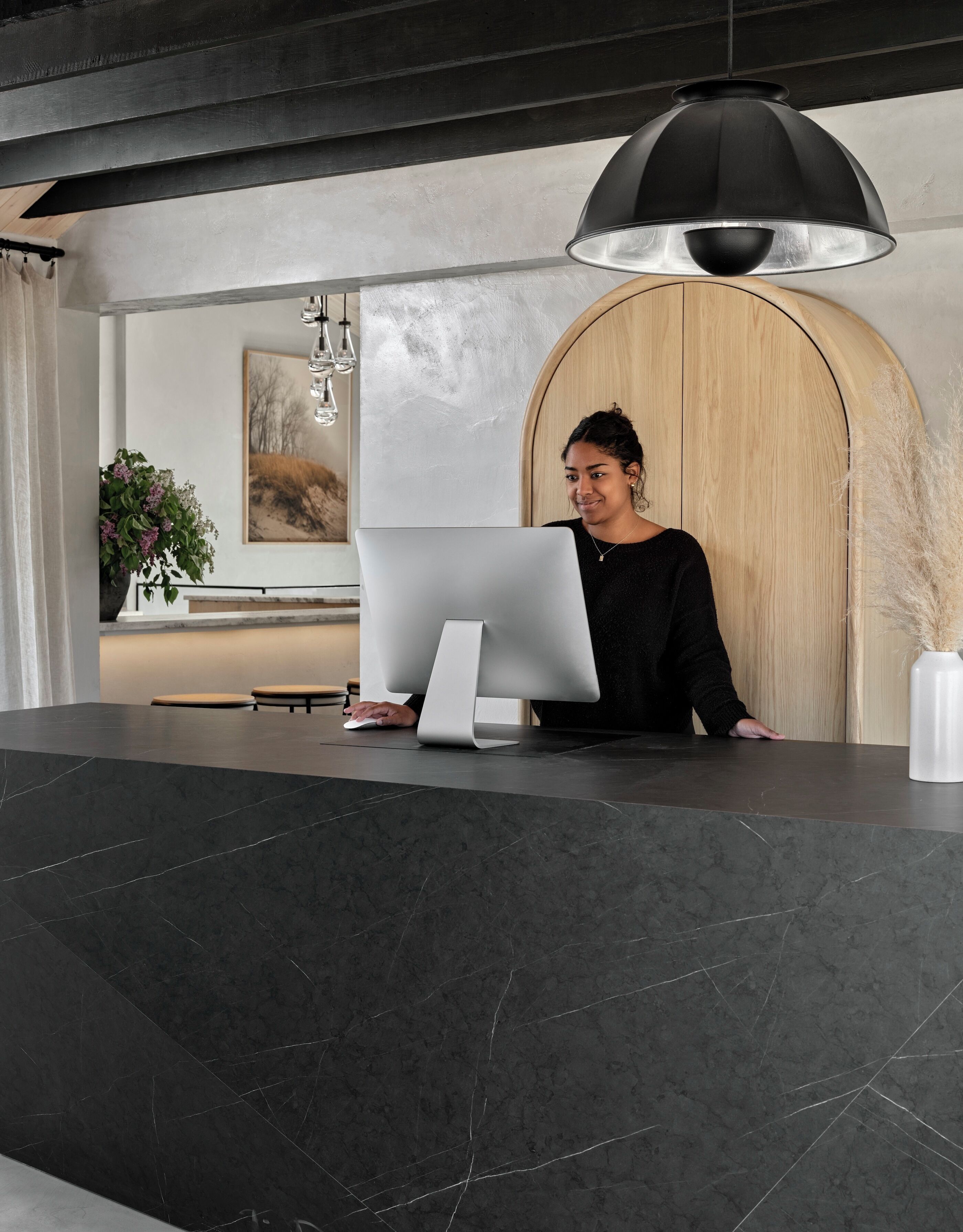 Een modern ontworpen receptiebalie met een groot scherm, toetsenbord en muis. Daarboven een houten paneel en een hangende lamp.