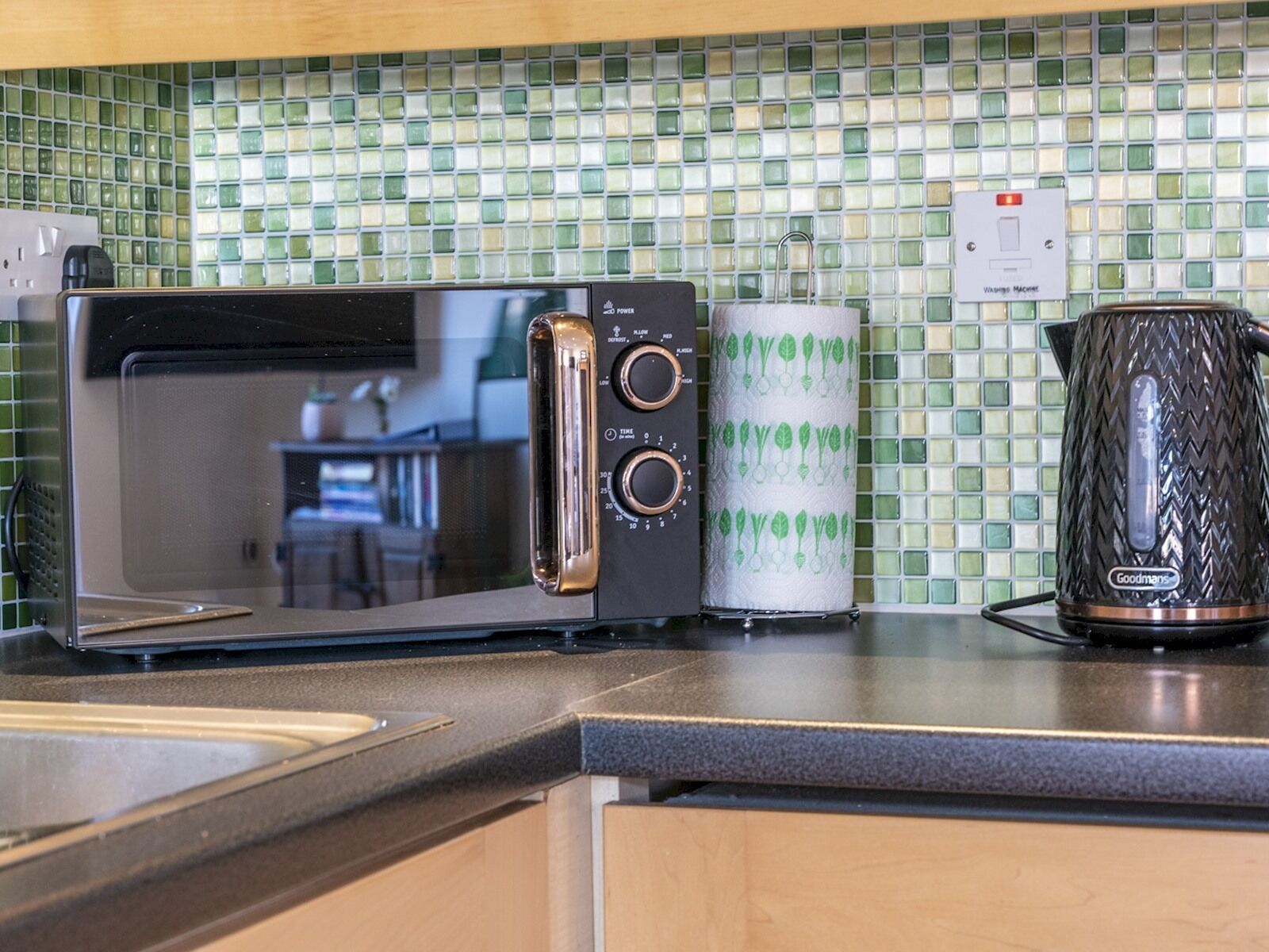 A kitchen with a toaster oven, a kettle, and a paper towel holder on the counter.