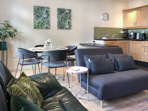 Una sala de estar moderna con un sofá gris, una mesa de comedor con sillas, y una zona de cocina con armarios de madera y un salpicadero de azulejos.
