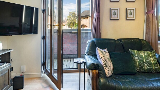A living room with a leather sofa, a flat-screen TV, and a sliding glass door leading to a balcony. - Stunning 2BR Apt with Balcony Next to Queens Uni - Pass the Keys (Belfast)