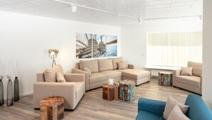 Un salon moderne avec un canapé d’angle, un divan bleu et des tabourets décoratifs en bois.
