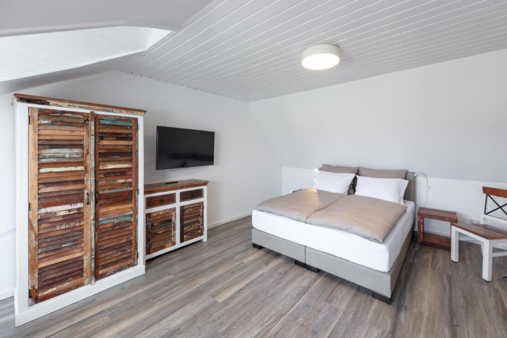 Une chambre à coucher avec un lit, une télévision, une armoire en bois et une petite table.