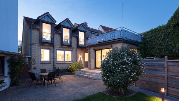 Une maison à deux étages avec un patio, un petit jardin et une clôture en bois.