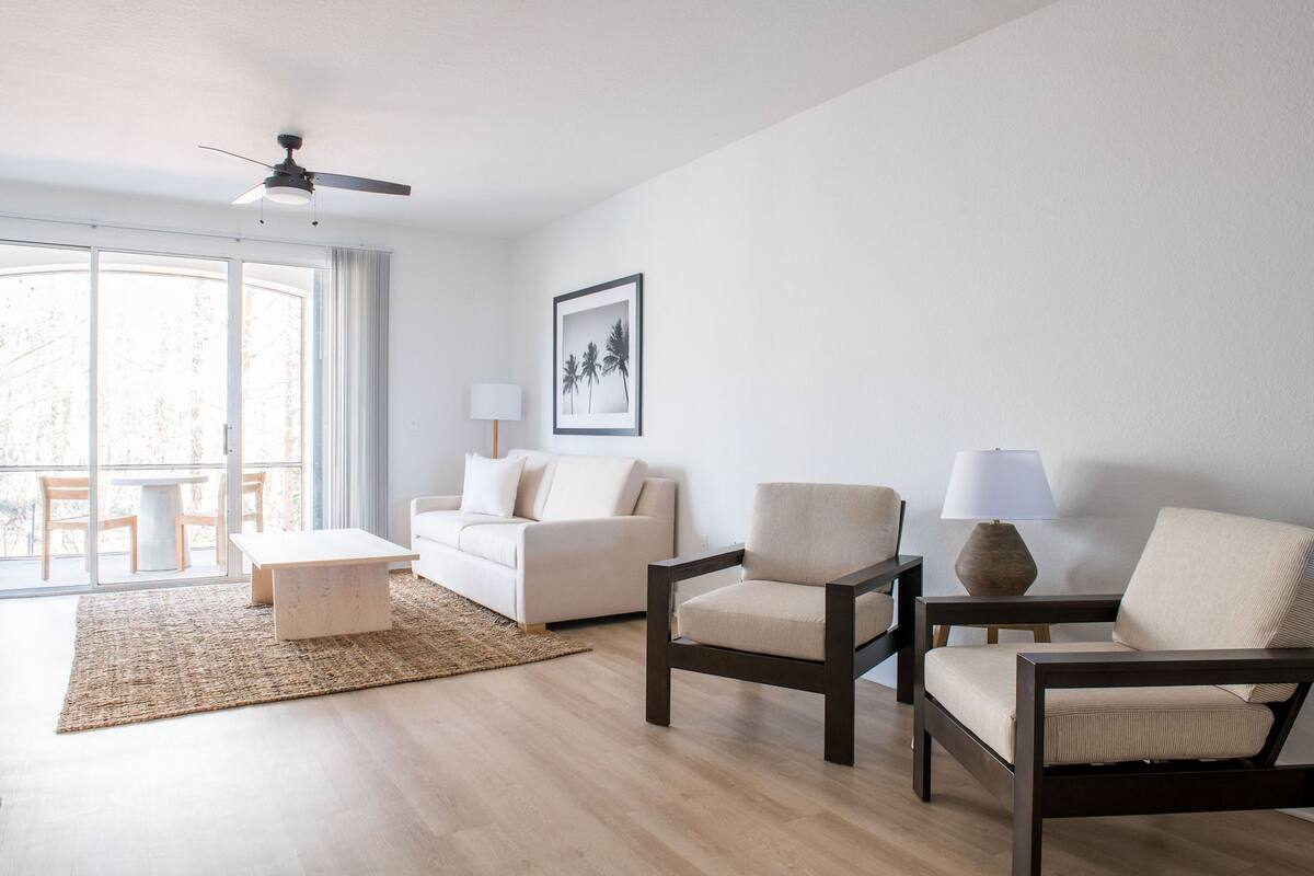 A modern living room with a sofa, two armchairs, a coffee table, a floor lamp, and a ceiling fan.
