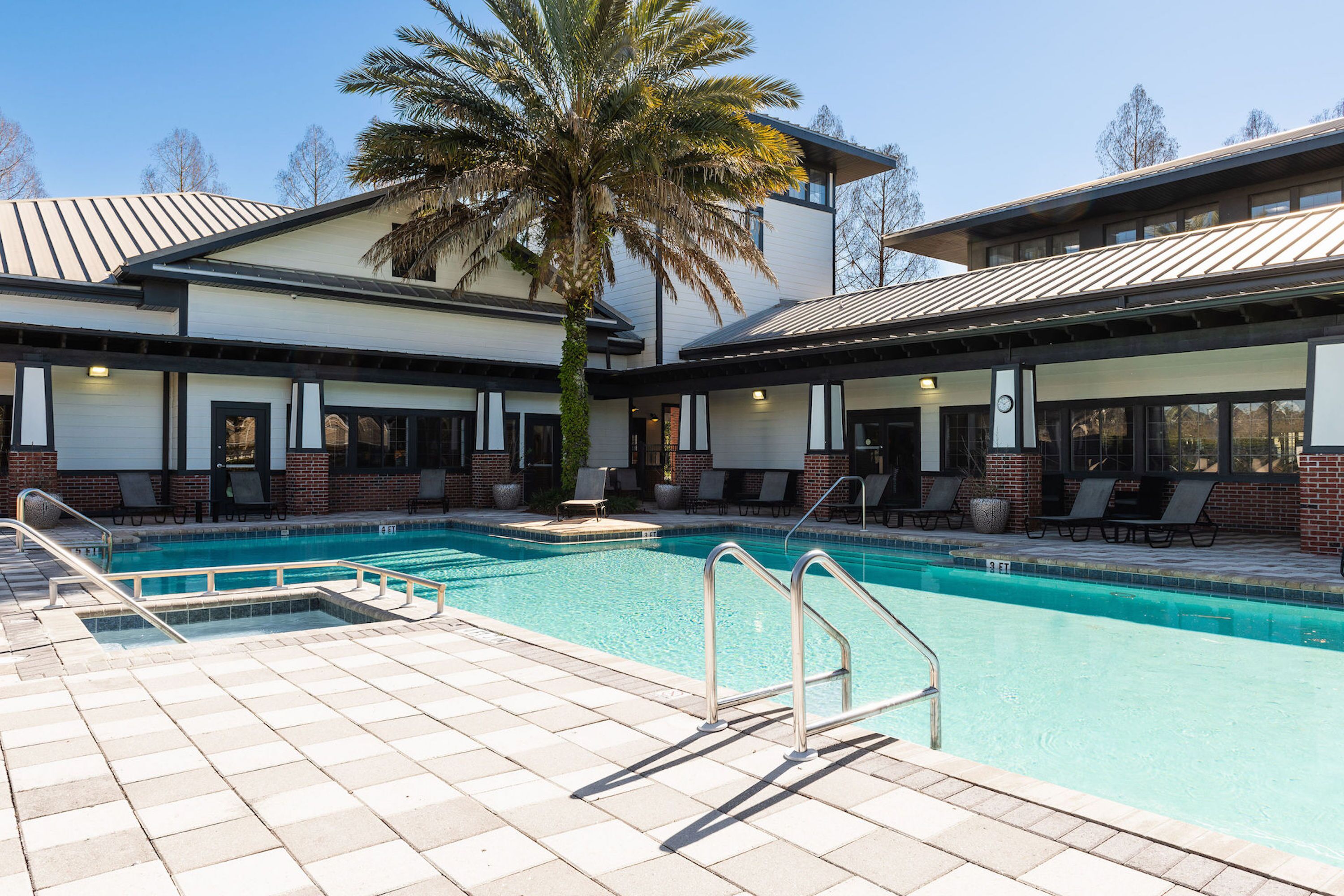 A pool area with a palm tree, lounge chairs, and a building with a modern design.