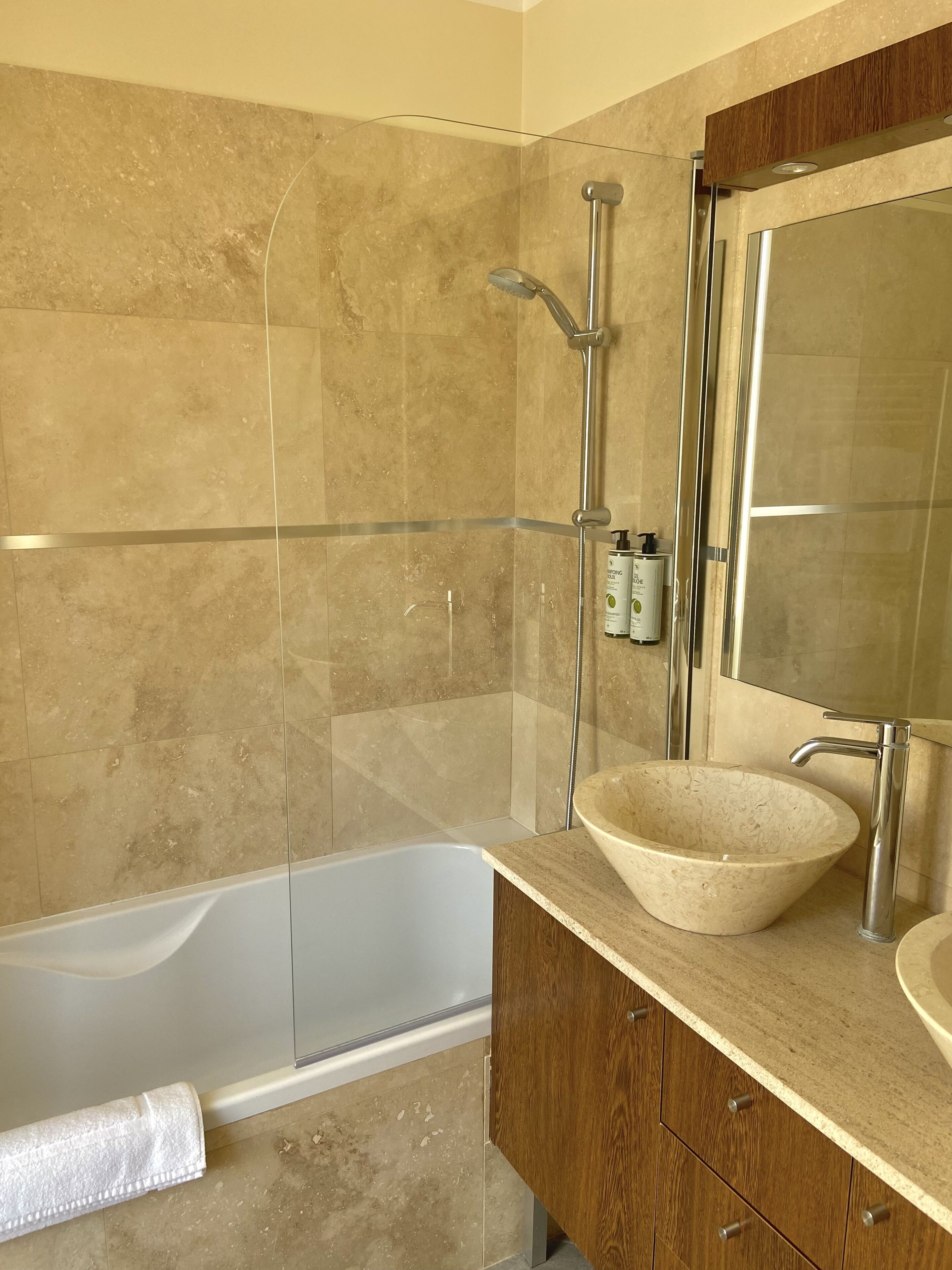 Een moderne badkamer met een bad, een douche met glazen wanden en een houten wastafelmeubel met een wastafel.