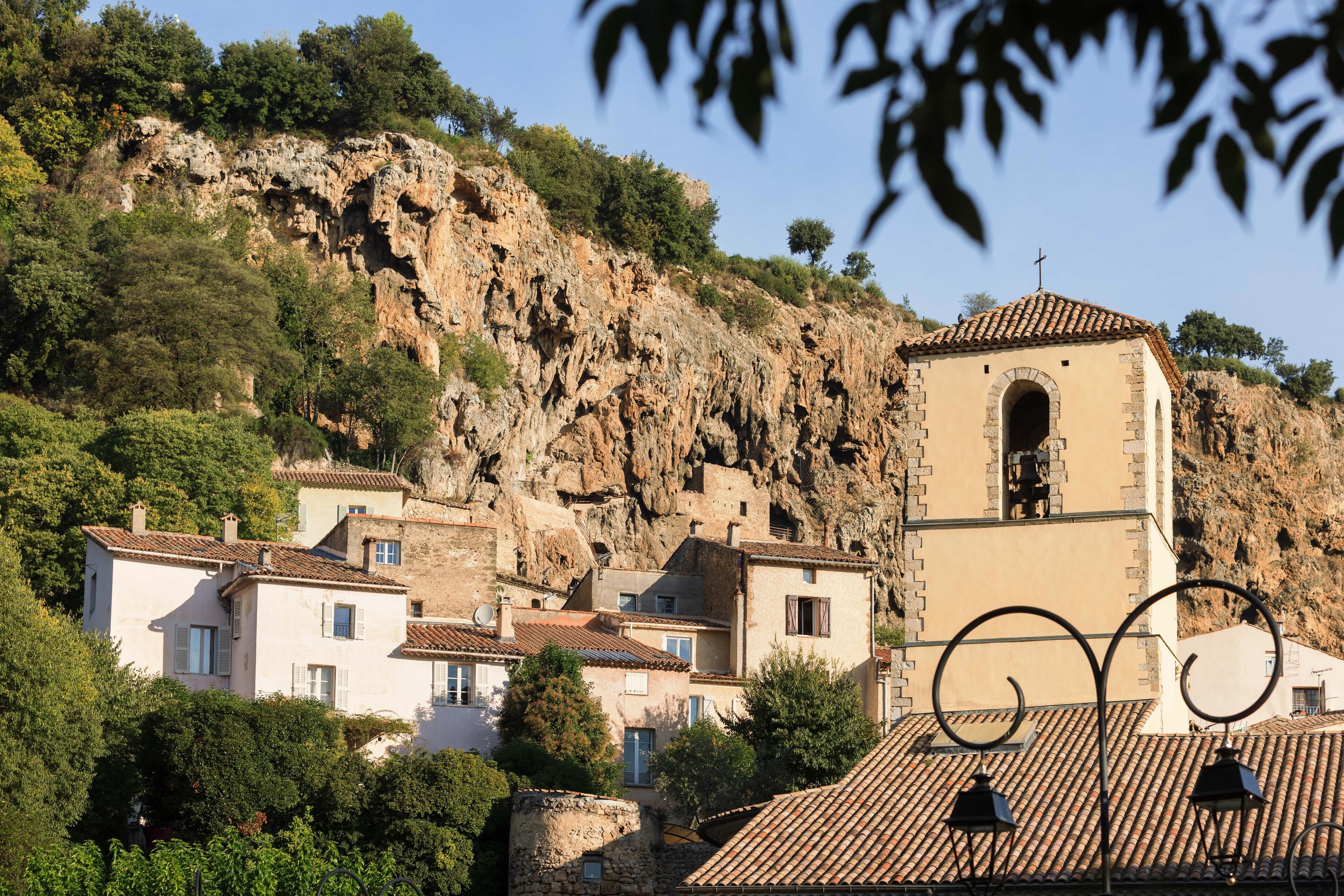 Un village aux bâtiments traditionnels en pierre, une église dotée d’un clocher et une colline rocheuse.