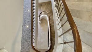 A spiral staircase with a wooden handrail and metal balusters, leading to a landing with a white wall and a fire extinguisher. - Hôtel La Falaise (Cotignac)