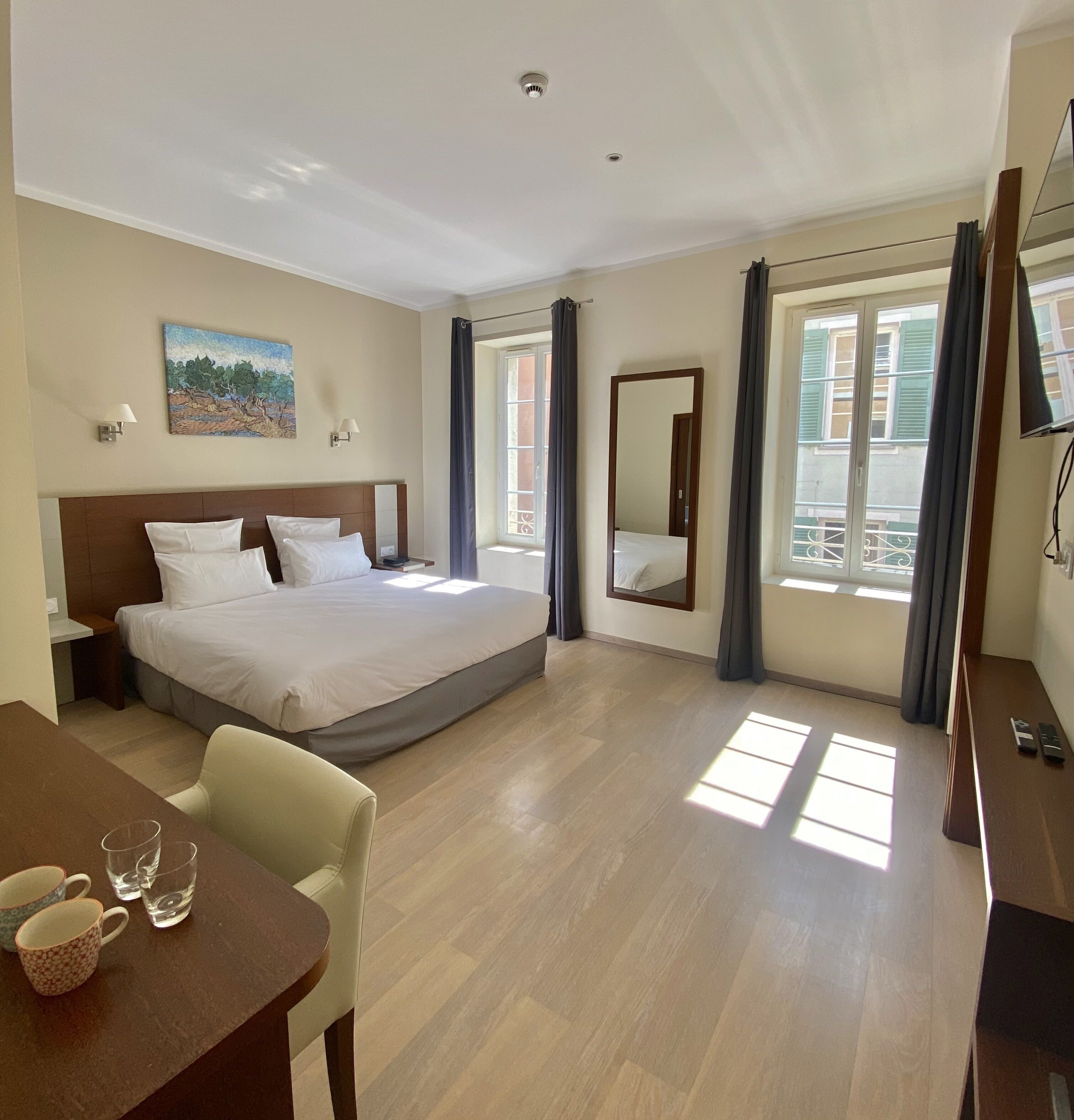Habitación de hotel con cama, mesita de noche, lámpara, un cuadro y vistas al exterior.