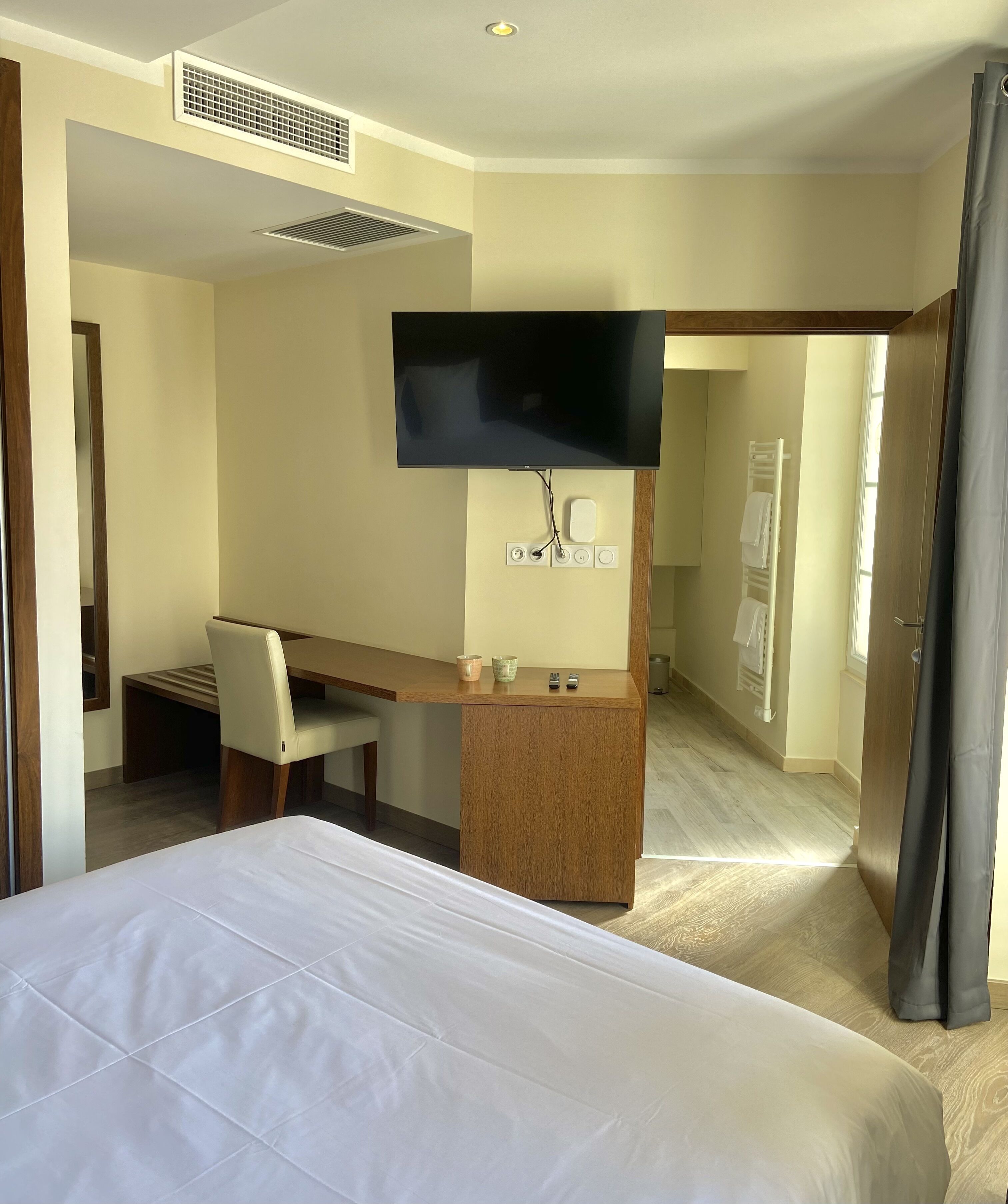 A hotel room with a bed, a desk, a chair, a television, and a window with curtains.