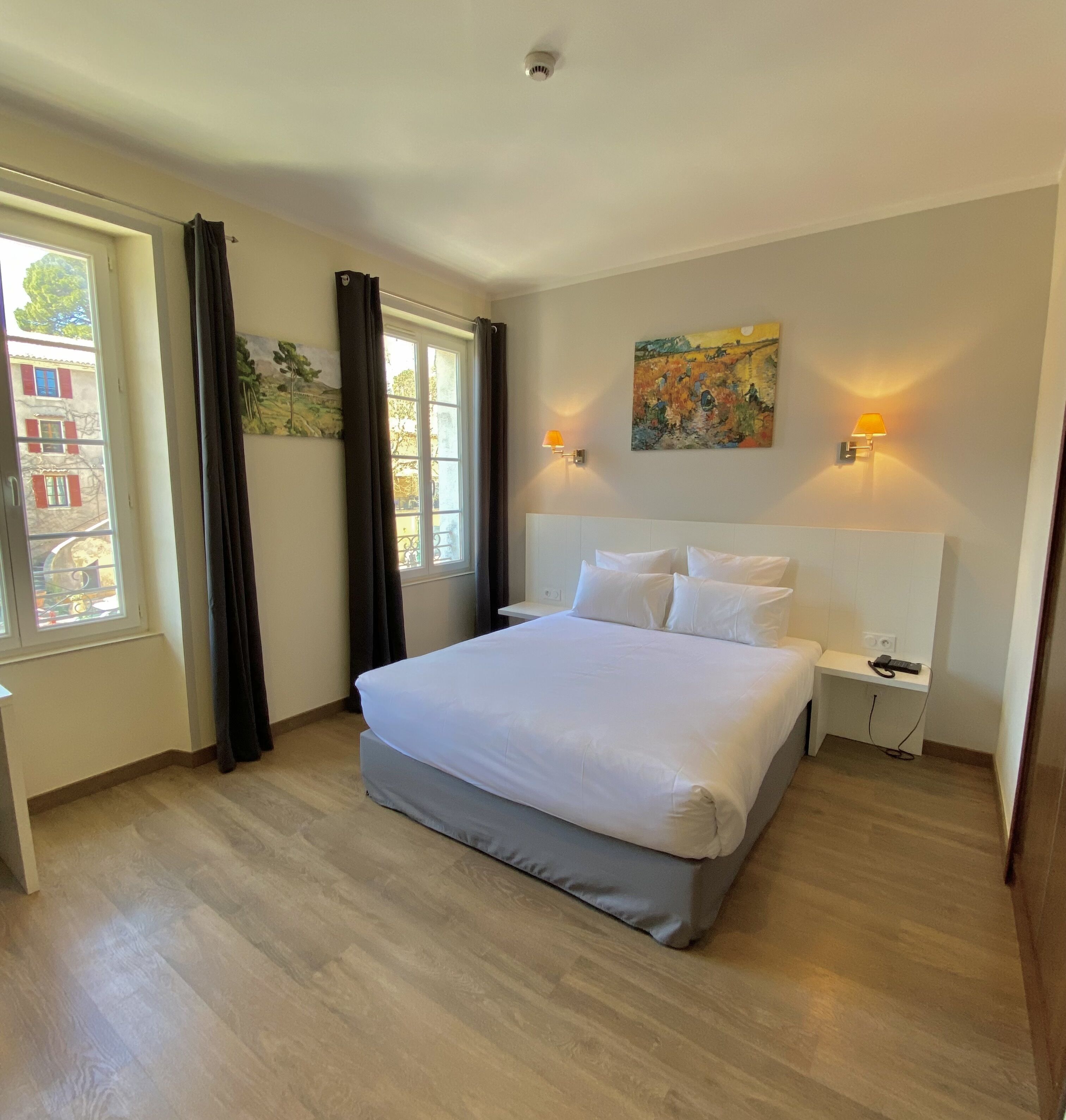 A bedroom with a large bed, two bedside tables, a painting on the wall, and a window with curtains.