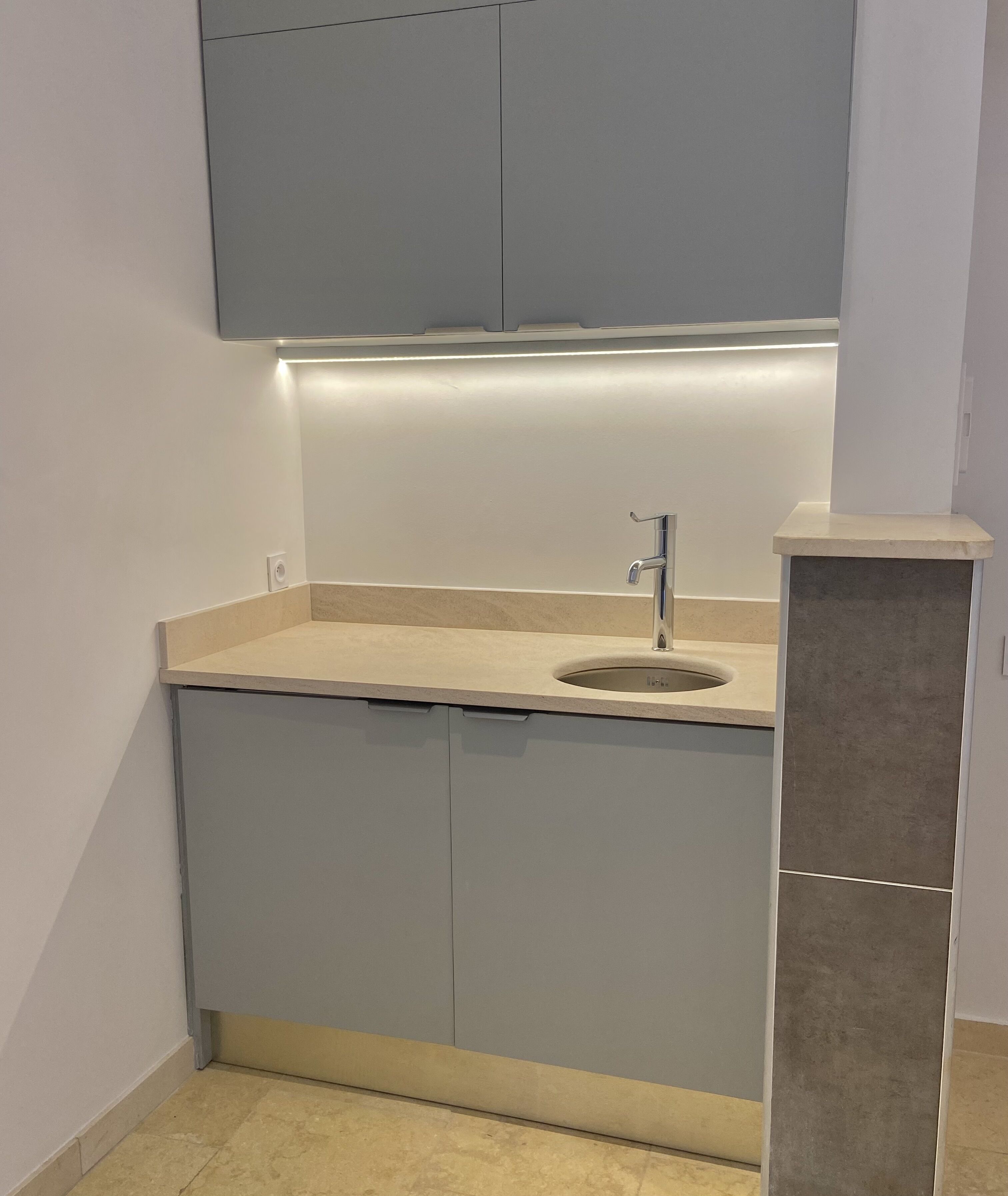 A modern kitchen with grey cabinets, a stainless steel sink, and a lighted countertop.