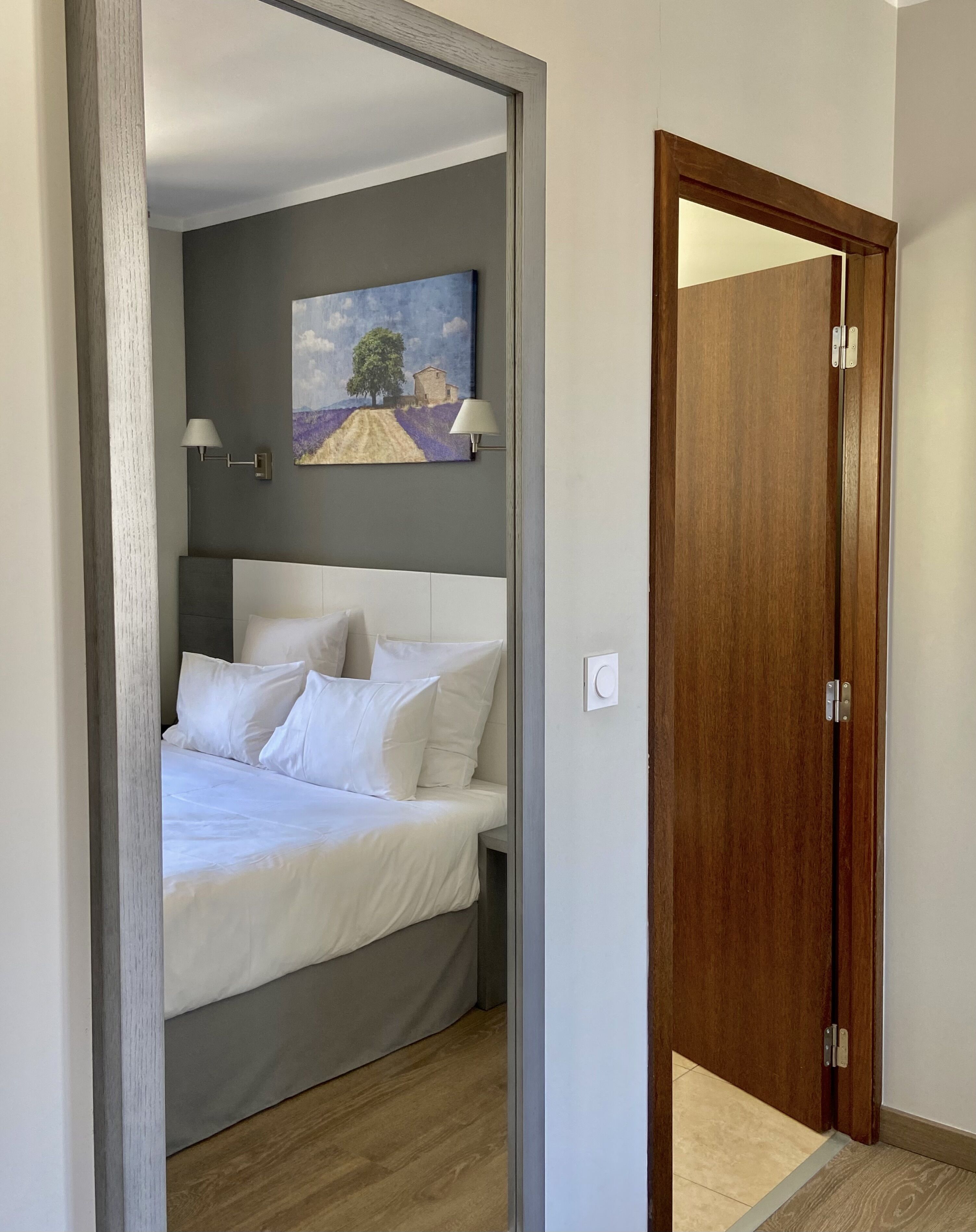 A bedroom with a bed, a painting, a nightstand, and a door.